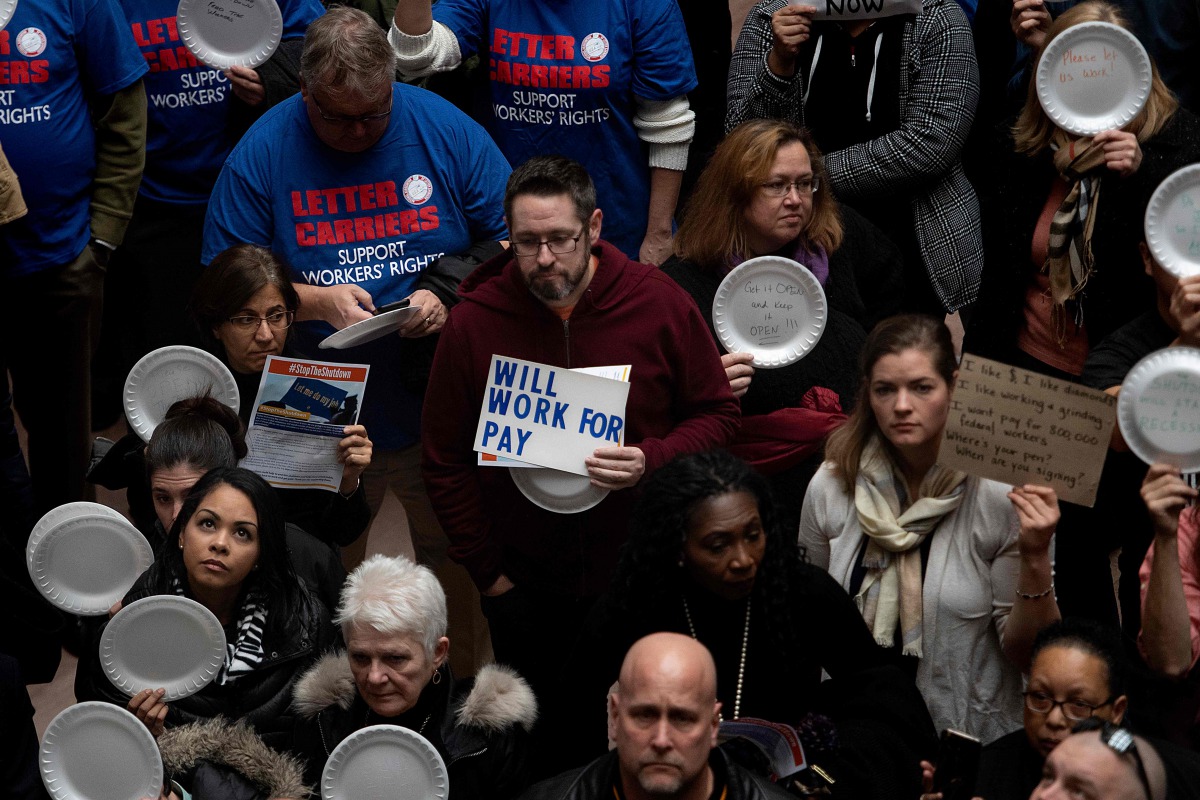 A federal worker stands with a placard reading 