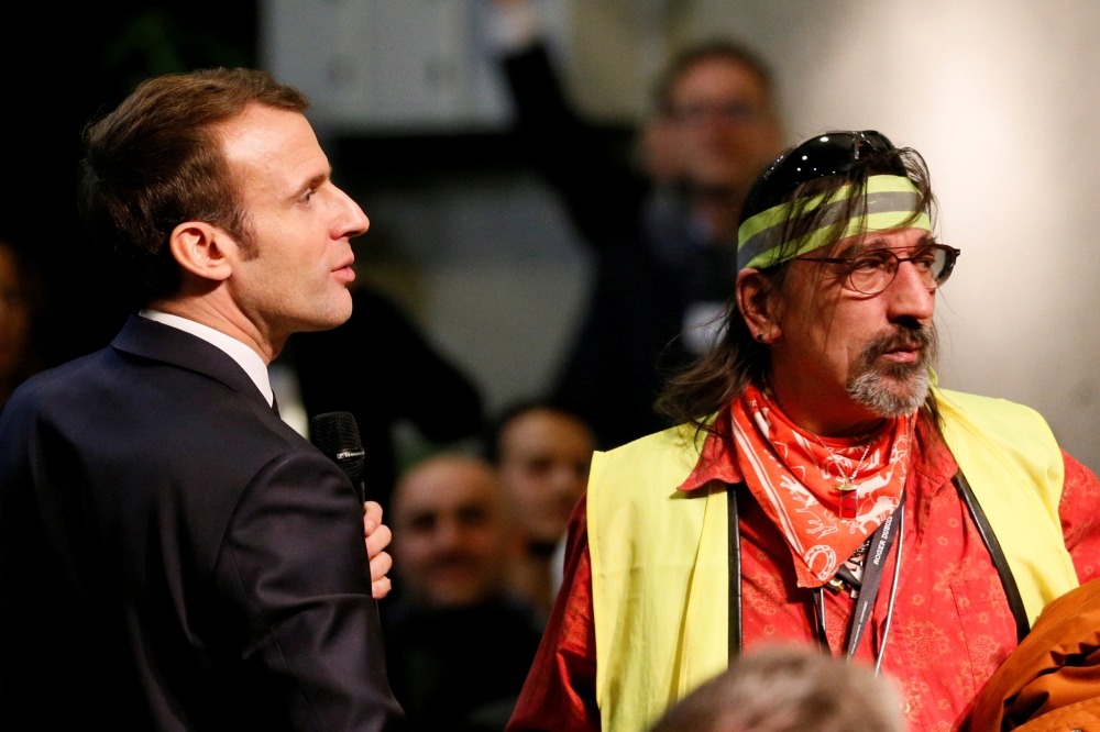 French President Emmanuel Macron stands near a man who wears a yellow vest as he attends a meeting with local residents as part of the 