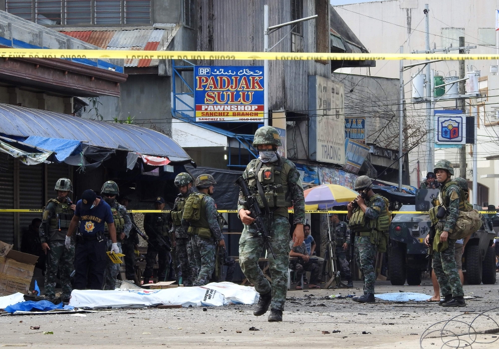 Policemen and soldiers keep watch as body bags (in white), containing the remains of blast victims, as seen in a cordoned area outside a church in Jolo, Sulu province on the southern island of Mindanao, on January 27, 2019. AFP / Nickee Butlangan 