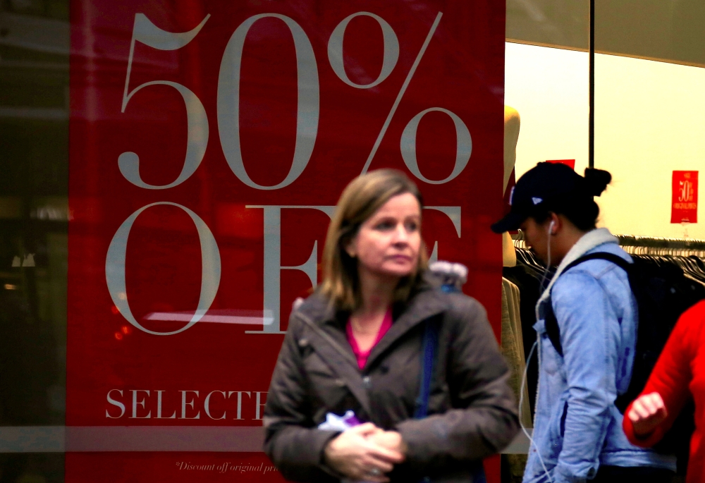 Shoppers walk in front of a retail shop displaying a sale sign in central Wellington, New Zealand, July 3, 2017. Reuters/David Gray
 