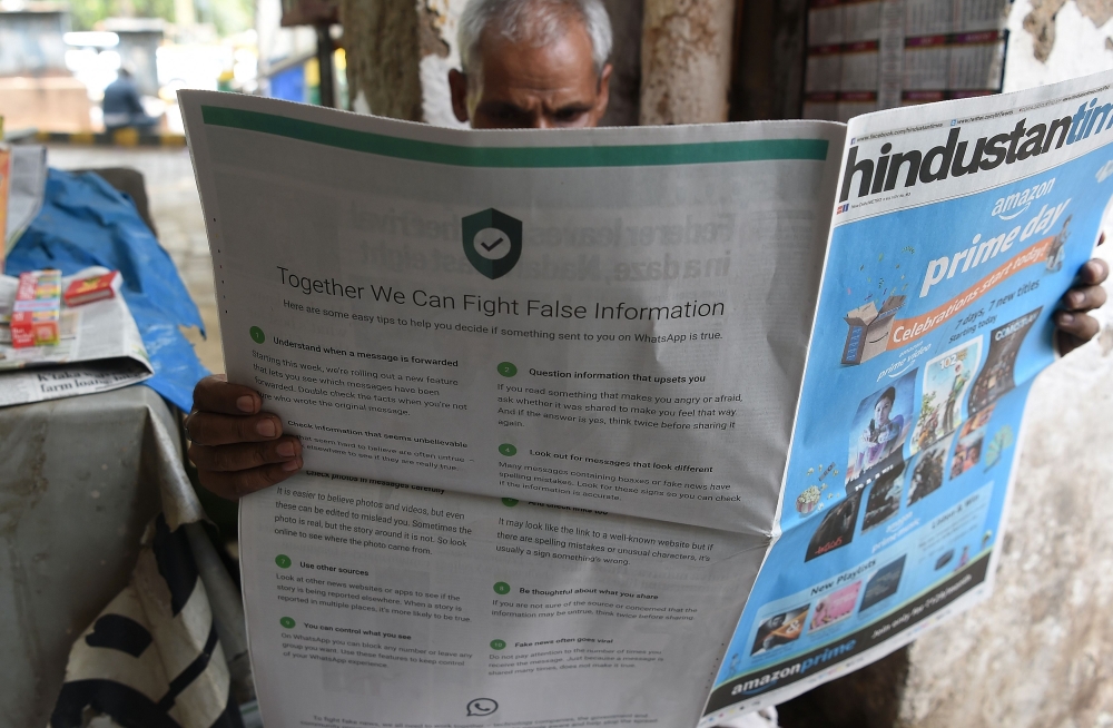 This photo illustration shows a newspaper vendor reading a newspaper with a full back page ad from WhatsApp intended to counter fake information in New Delhi on July 10, 2018. AFP / Prakash Singh