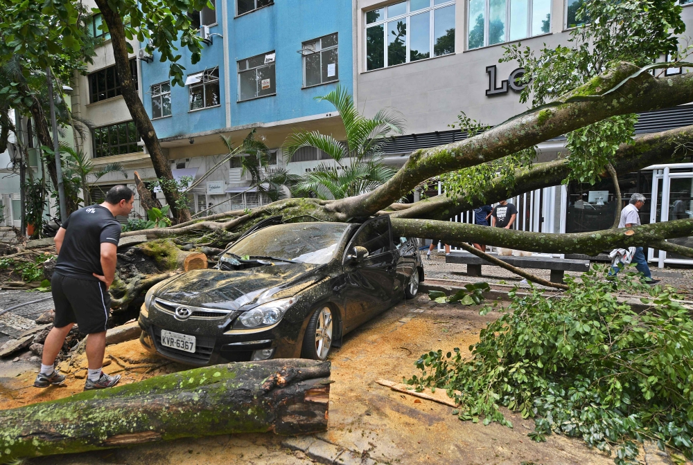 The owner looks at his car damaged by a fallen tree after a storm in Rio de Janeiro, Brazil, on February 7, 2019.  AFP / CDS / Carl De Souza  