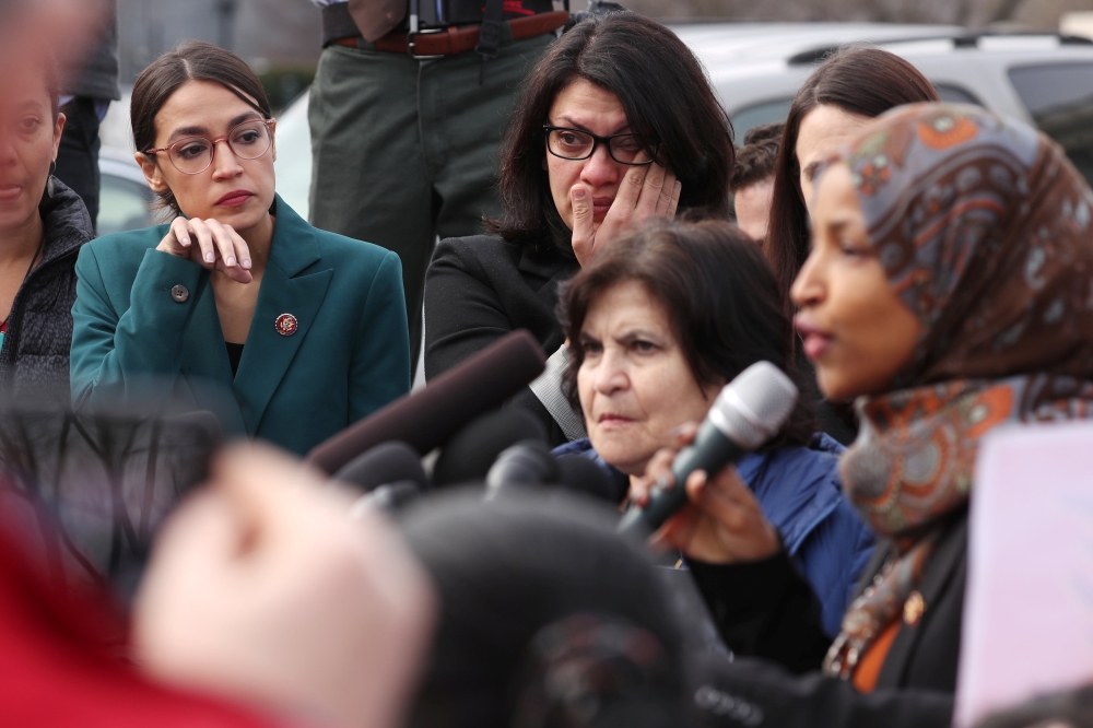 US Representative Alexandria Ocasio-Cortez (D-NY) and Representative Rashida Tlaib (D-MI) wipe away tears as Representative Ilhan Omar (D-MN) talks about her own experience as a refugee during a news conference to call on Congress to cut funding for ICE (