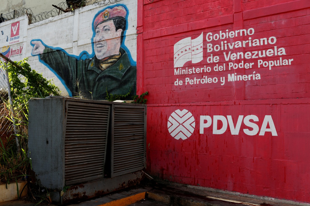 The logo of the Venezuelan state oil company PDVSA is seen next to a mural depicting late President Hugo Chavez at a gas station in Caracas, March 2, 2017. Reuters/Carlos Garcia Rawlins