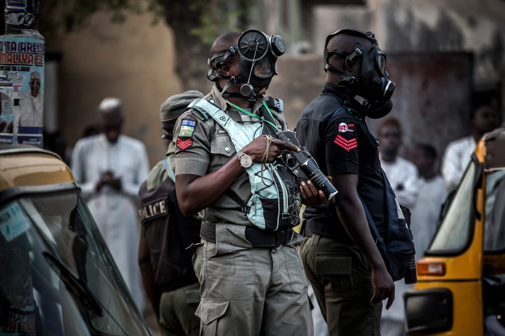 Nigerian police wearing gas masks monitor an area where All Progressives Congress Party (APC) supporters celebrate initial results released by the Nigerian Independent National Electoral Commission (INEC) in Kano, on February 25, 2019, two days after gene
