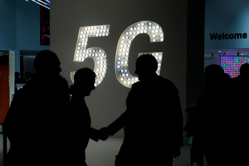 Visitors shake hands next to a 5G hotspot sign at the Mobile World Congress (MWC) in Barcelona on February 27, 2019.  AFP / Pau Barrena  