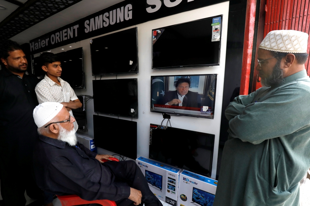 Shopkeepers watch the speech of Pakistani Prime Minister Imran Khan. REUTERS/Akhtar Soomro