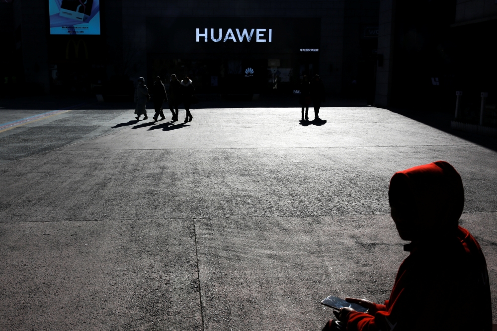 A man uses his phone as he sits in front of a Huawei shop in Beijing, December 11, 2018. Reuters/Thomas Peter