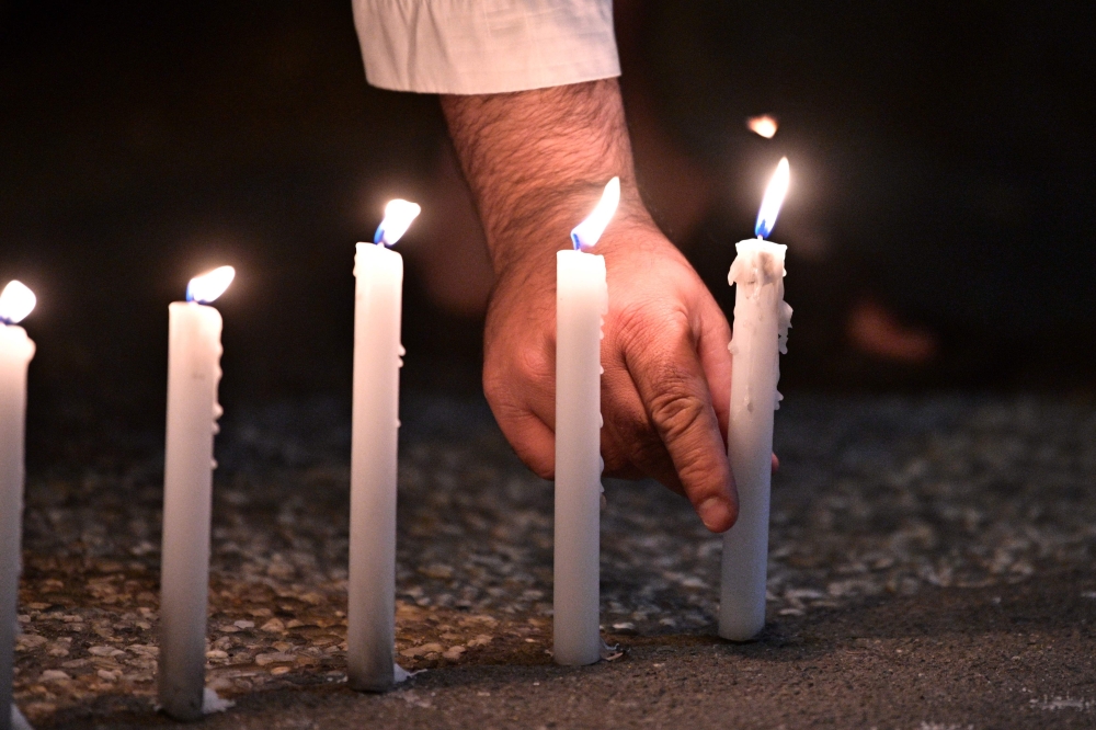 A well-wisher helps to light 49 candles as he pays respects to victims outside the hospital in Christchurch on March 16, 2019, after a shooting incident at two mosques in the city the previous day. AFP / Anthony WALLACE