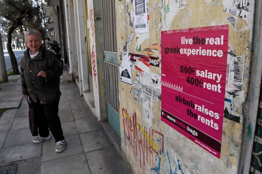 A woman walks past a poster in the Koukaki area in Athens, which in 2016 was named Airbnb's fifth fastest growing neighbourhood globally with an 800-percent jump in home-sharing. AFP/Louisa Gouliamaki