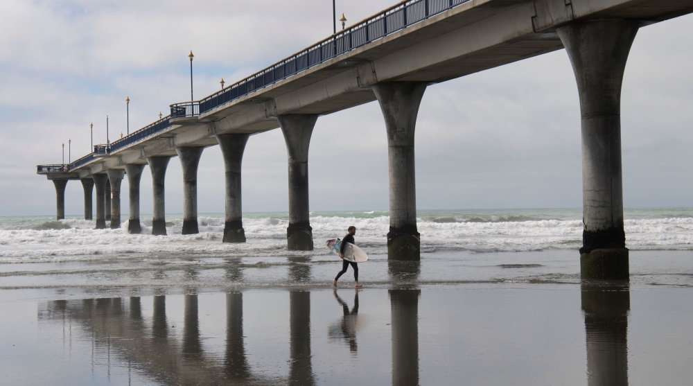 A surfer runs under the New Brighton Pier in Christchurch on March 24, 2019, as the city attempts to resume normal life after the shootings in local mosques. AFP / William West 