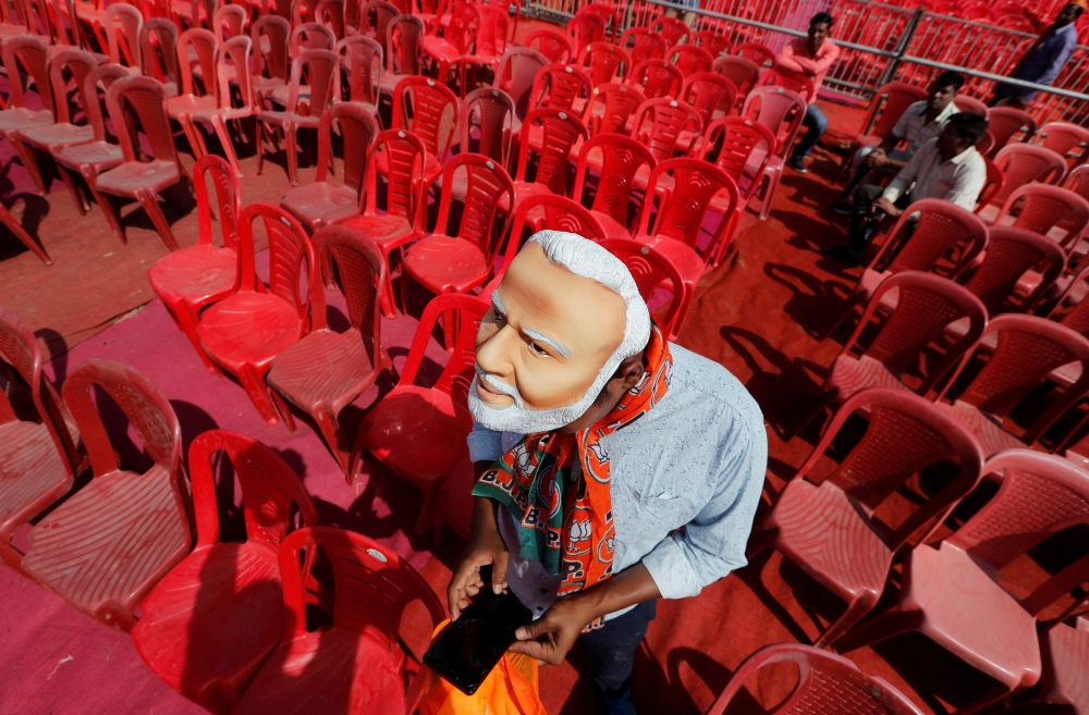 A supporter of India's ruling Bharatiya Janata Party (BJP) wearing a mask of Narendra Modi checks his mobile phone as he attends an election campaign rally being addressed by Modi in Meerut in the northern Indian state of Uttar Pradesh, India, March 28, 2