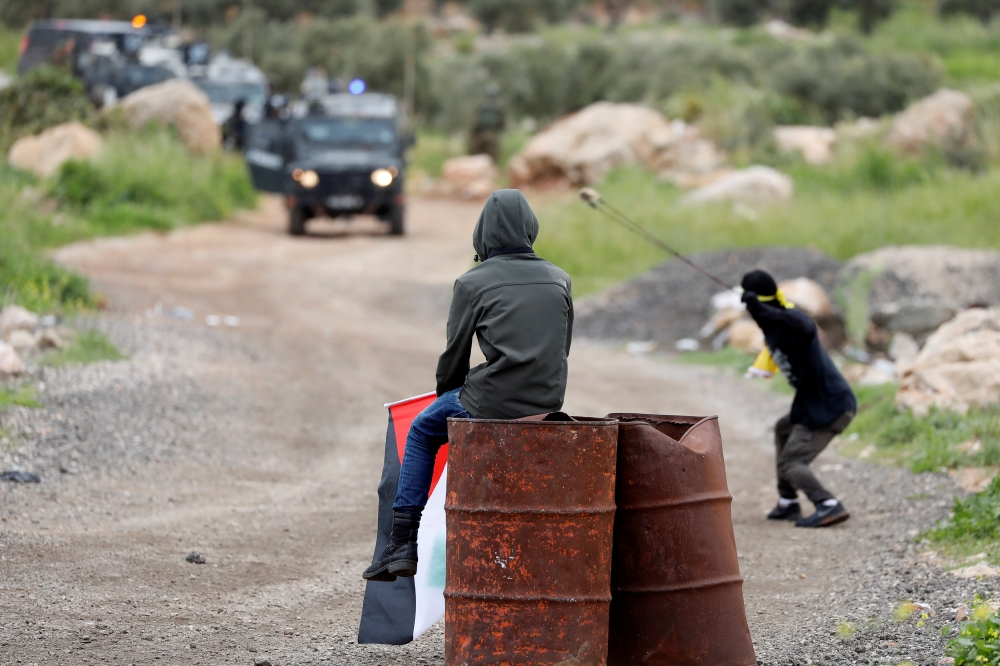 A Palestinian watches as other hurls stones at Israeli troops during a protest marking the Land Day in al-Mughayer village, in the Israeli-occupied West Bank March 29, 2019. Reuters/Mohamad Torokman