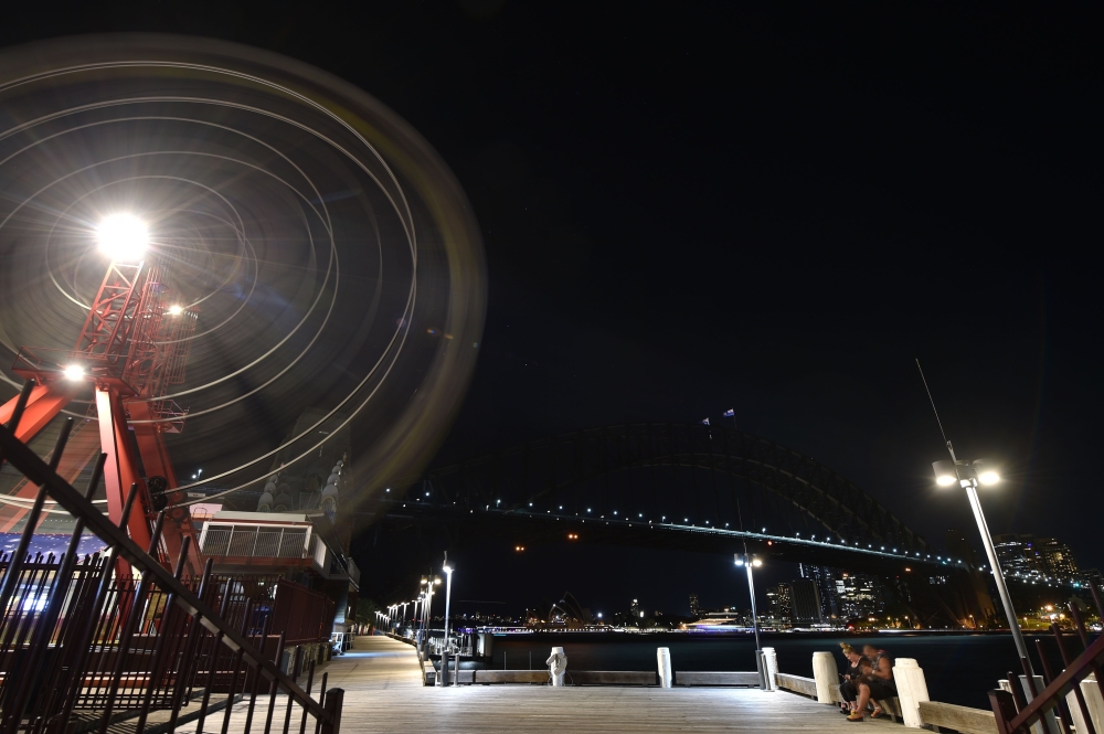 The Sydney Harbour Bridge, the Opera House and the ferris wheel are seen after their lights went out as seen from Sydney's Luna Park for the Earth Hour environmental campaign on March 30, 2019.  AFP / PETER PARKS