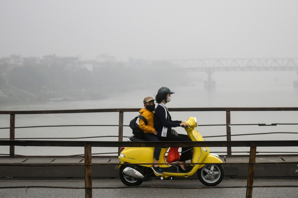 A Vietnamese woman wearing a face mask rides on a bridge amidst a blanket of smog over Hanoi on March 28, 2018. AFP / Manan Vatsyayana 