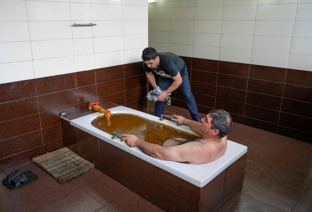 A man bathes in a tub filled with Naftalan crude oil during a treatment session at Sehirli Naftalan Health Center, some 300 kilometres from Baku, on March 21, 2019.  AFP / Mladen Antonov 