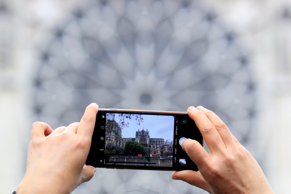 A man takes pictures of Notre-Dame Cathedral after a massive fire devastated large parts of the gothic gem in Paris, France April 16, 2019. Reuters/Gonzalo Fuentes