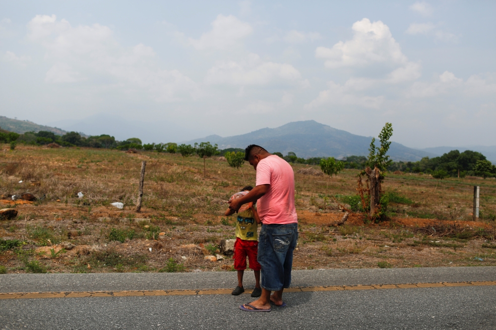 A Honduran migrant hydrates his son in the middle of a road as they walk with other Central American migrants during their journey towards the United States, in Escuintla, Mexico April 18, 2019. REUTERS/Jose Cabezas