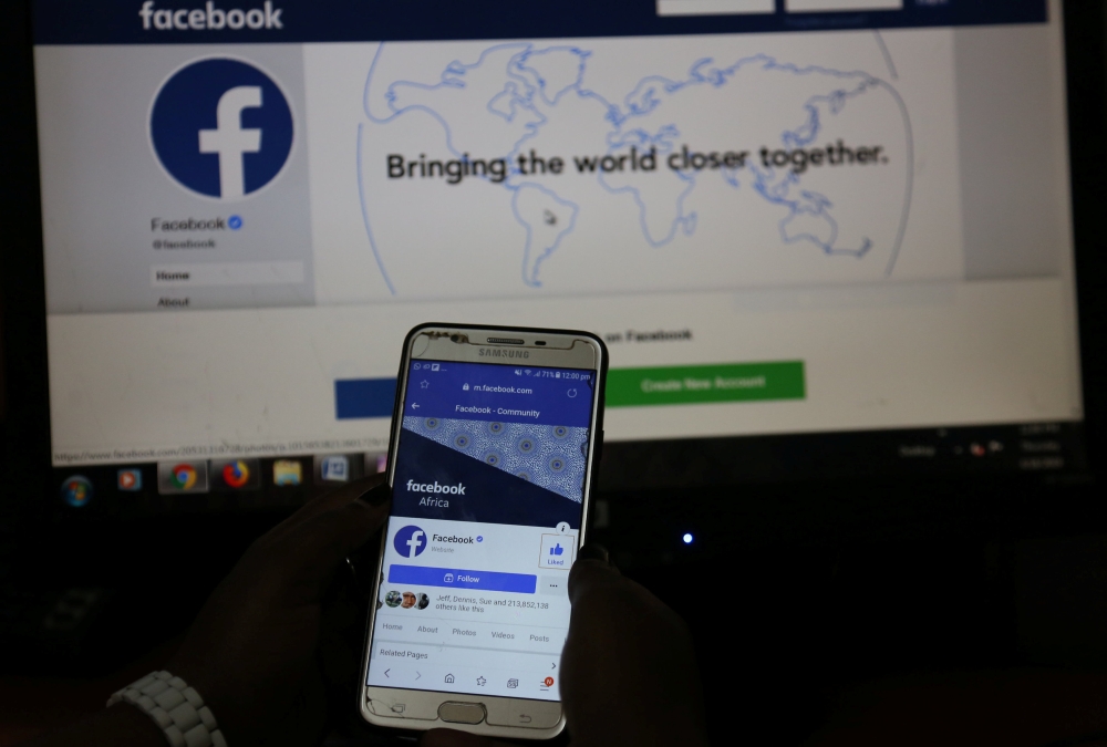 An illustration photo shows the Facebook page displayed on a mobile phone held in front of a computer screen at a cyber-cafe in downtown Nairobi, Kenya April 18, 2019. Reuters/Stringer