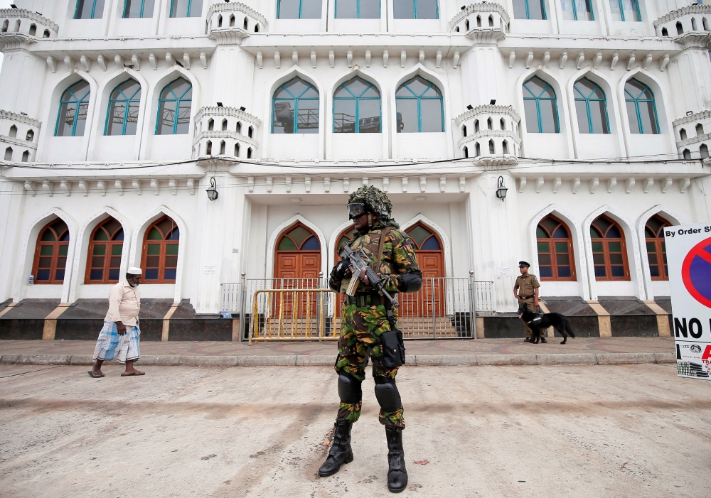 Sri Lankan Special Task Force soldiers stand guard in front of a mosque as a Muslim man walks past him during the Friday prayers at a mosque, five days after a string of suicide bomb attacks on Catholic churches and luxury hotels across the island on East