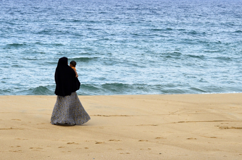In this picture taken on April 25, 2019, a Sri Lankan Muslim woman walks along a beach with her child in Kattankudy. AFP / Lakruwan Wanniarachchi