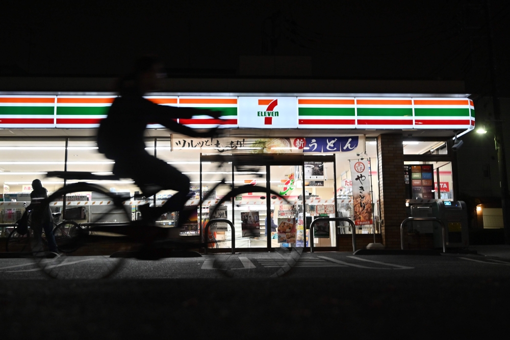 This photo taken on April 21, 2019 shows a cyclist passing a 7-Eleven convenience store at night in Tokyo. AFP / Charly Triballeau