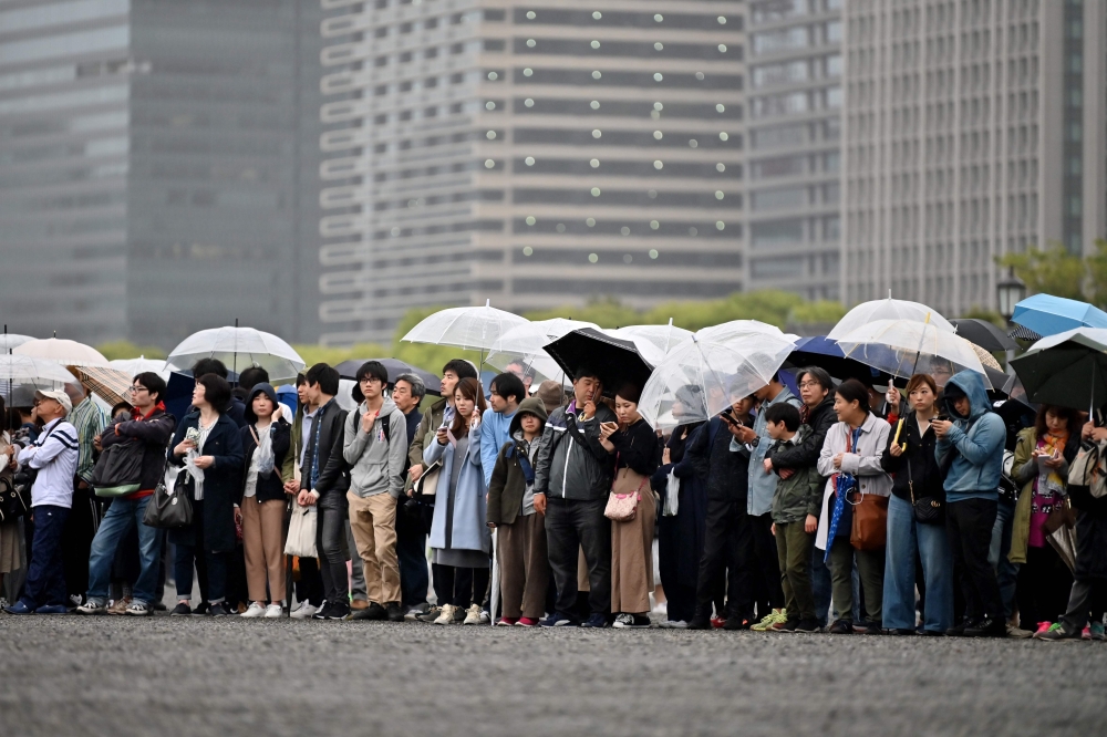 People hold umbrellas to shelter themselves from the rain as they gather outside the Imperial Palace, where the abdication ceremony for Japan's Emperor Akihito will take place, in Tokyo on April 30, 2019.  AFP / Charly TRIBALLEAU