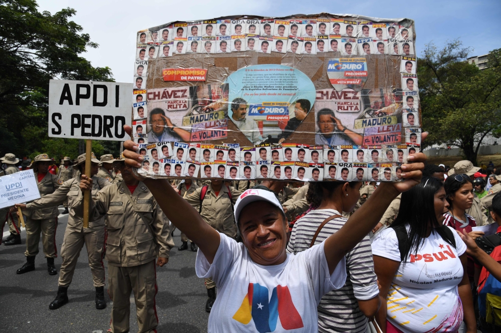 Supporters of Venezuelan President Nicolas Maduro display placard with pictures of Maduro and late leader Hugo Chavez during a rally on May Day in Caracas on May 1, 2019.   AFP / Yuri CORTEZ