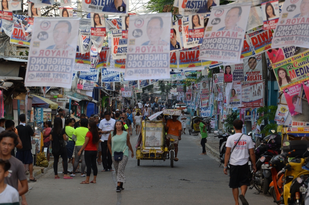 Residents walk past posters of candidates for the midterm elections near a polling precinct in Manila on May 13, 2019. AFP / TED ALJIBE