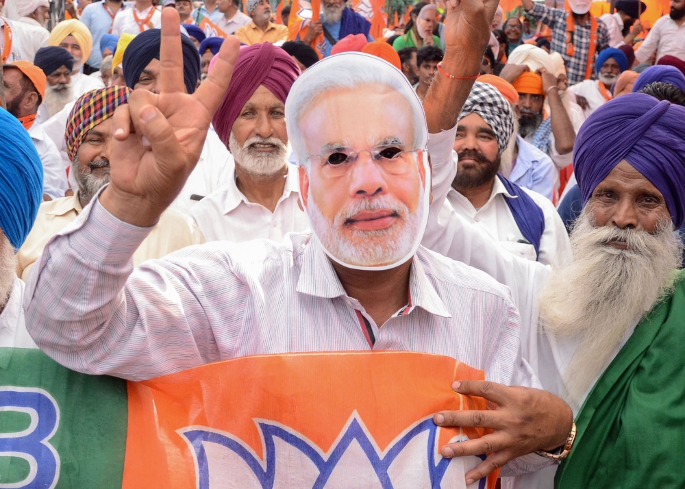 File photo of an Indian BJP supporter wearing a mask of Indian Prime Minister Narendra Modi gestures during an election rally in Amritsar on May 12, 2019. / AFP / NARINDER NANU 