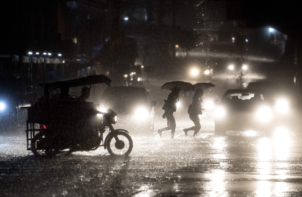 People cross a road during heavy rain caused by Typhoon Maliksi in Manila on June 10, 2018. AFP/Noel Celis