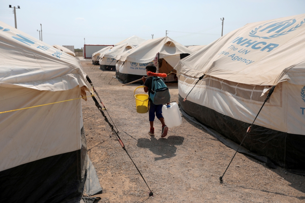 FILE PHOTO: A Venezuelan migrant child carries a broom and a bucket while he walks in a camp run by the UN refugee agency UNHCR in Maicao, Colombia May 7, 2019. Picture taken May 7, 2019. REUTERS/Luisa Gonzalez