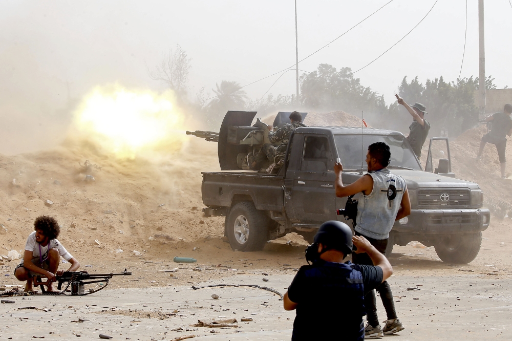 A fighter loyal to the Libyan internationally-recognised Government of National Accord (GNA) fires a heavy machine gun as a press photographer take pictures of the scene during clashes against forces loyal to strongman Khalifa Haftar, on May 25, 2019, in 
