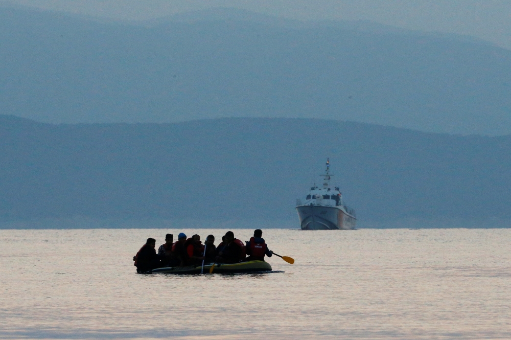 Migrants in a dinghy paddle their way on the Mediterranean Sea to attempt crossing to the Greek island of Kos, as a Turkish Coast Guard ship patrols off the shores off Bodrum, Turkey, September 19, 2015. Reuters/Umit Bektas