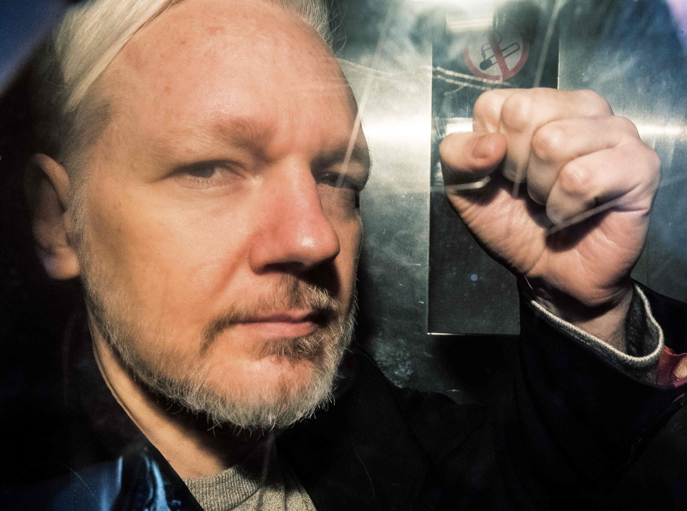 In this file photo taken on May 01, 2019 WikiLeaks founder Julian Assange gestures from the window of a prison van as he is driven out of Southwark Crown Court in London, after having been sentenced to 50 weeks in prison for breaching his bail conditions 
