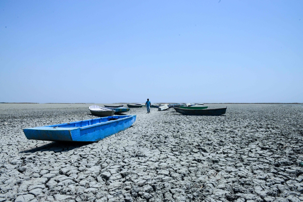 In this picture taken on June 4, 2019, an Indian boatman walks amid boats on the dried bed of a lake at Nalsarovar Bird Sanctuary, on the eve of World Environment Day. AFP / Sam Panthaky 