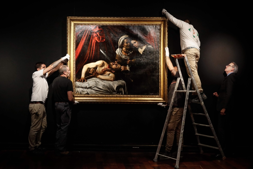 Workers hang on a wall a painting believed by some experts to be Caravaggio's 