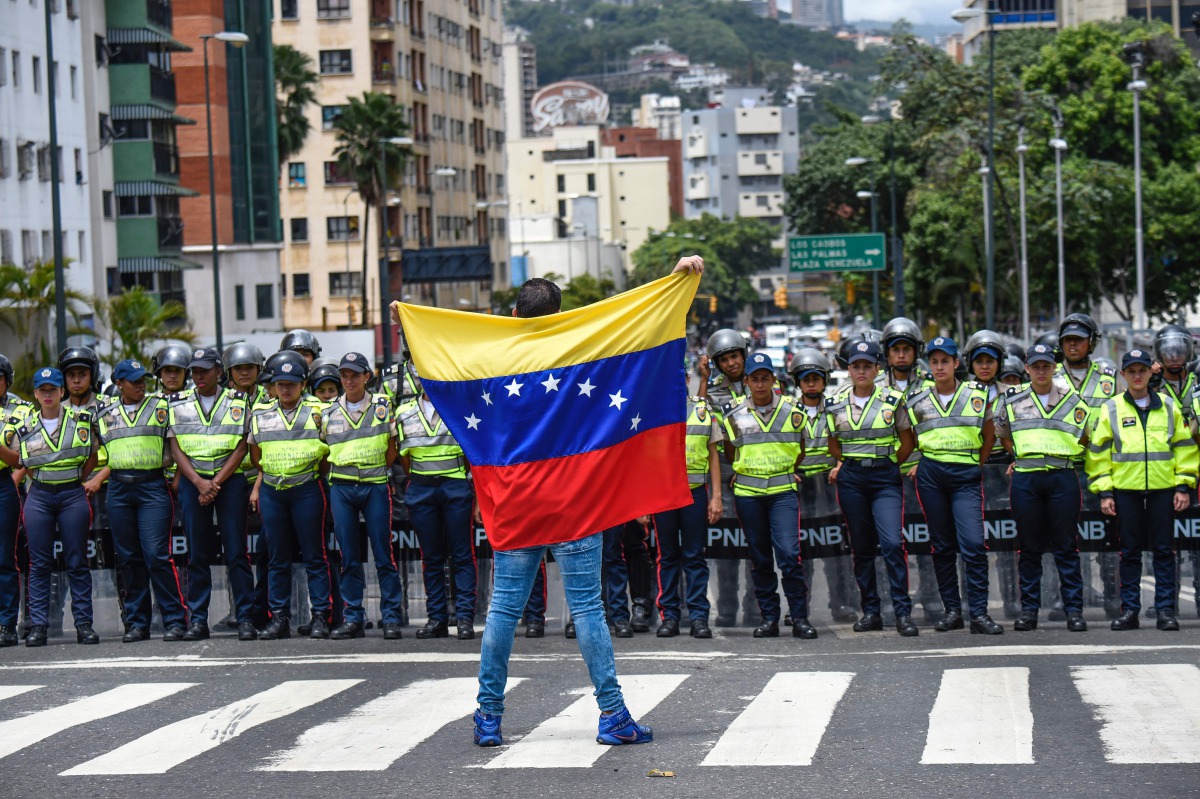 A member of the Venezuela opposition gestures showing a national flag in front of National policemen during a demonstration in Caracas on July, 27, 2016 (AFP) 
