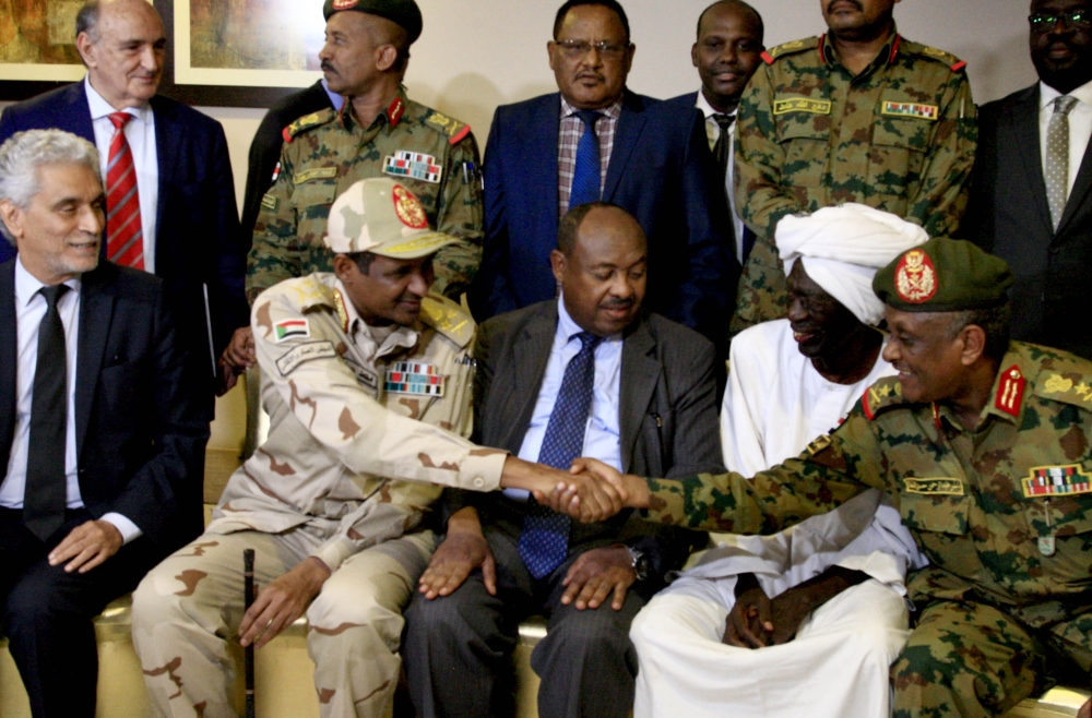 African union envoy to Sudan Mohamed al-Hacen Lebatt (L) sits next to Sudan's deputy chief of the ruling military council General Mohamed Hamdan Dagalo as he shakes hands with an army general following a press conference in Khartoum in which they announce