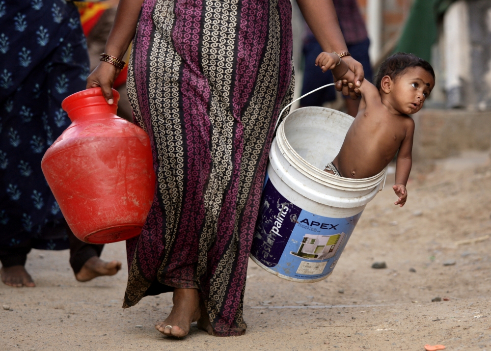 A woman carries her son in a bucket after collecting water from a municipal water tanker on the outskirts of Chennai, India, July 4, 2019. (REUTERS/P. Ravikumar)