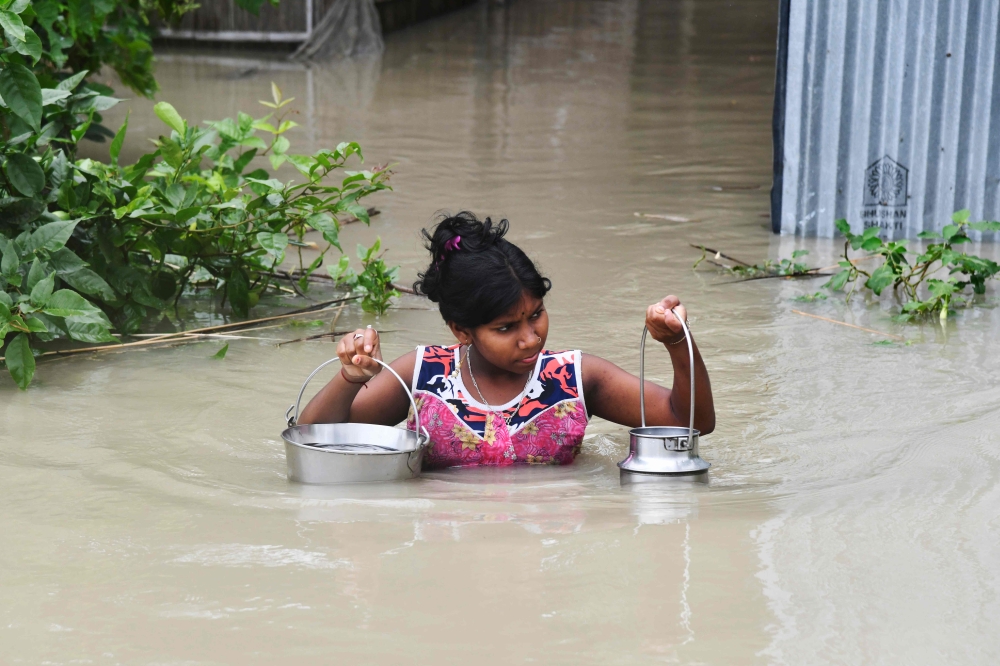 An Indian girl carries drinking water as she wades through flood waters at Pabhokathi village in Morigaon district of India's Assam state on July 15, 2019. AFP / Biju Boro 