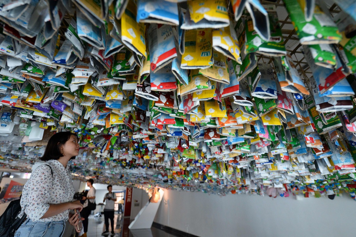 Visitors view a hanging art installation by a group of artists made from scraps of plastics, cans and containers at an exhibition 