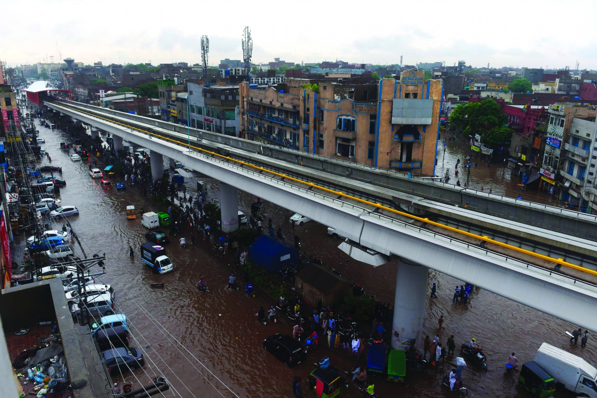 Pakistani commuters and pedestrians cross a flooded street after heavy monsoon rains in Lahore on July 16, 2019. In Pakistan-administered Kashmir, officials said at least 23 people were killed after heavy rain triggered flash floods and damaged more than 