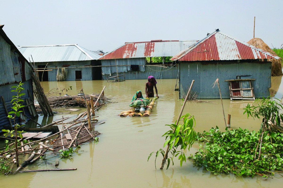 People walk in floodwaters as they transport belongings on a makeshift raft following heavy monsoon rains at a flood affected area of Gaibandha District, in Northern Bangladesh, on July 19, 2019. AFP / Rehman Asad
