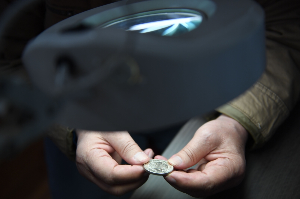 An archaeologist, Hungarian Ferenc Redo examines a metal coin of a Holocaust victim's collection in the Balatoni Museum in the town of Keszthely, 200 km west of Budapest on May 22, 2019. AFP/Attila Kisbenedek