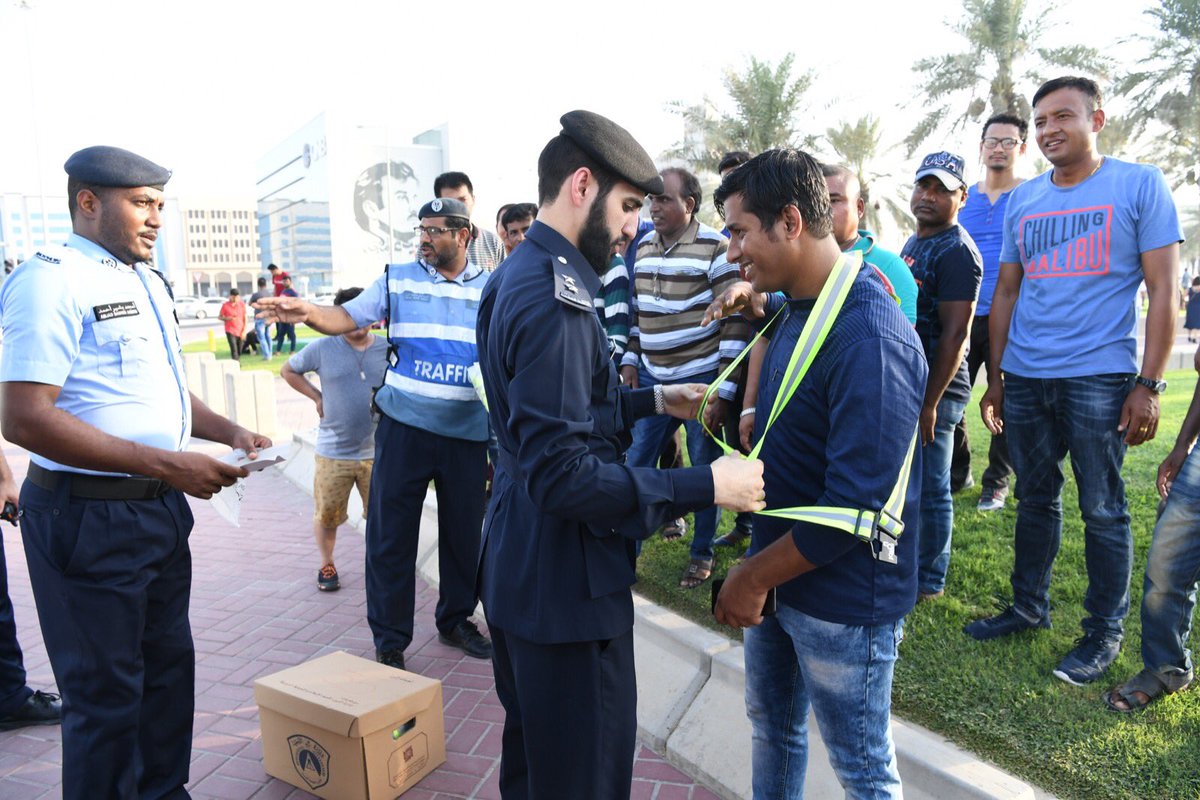 A traffic police officer giving reflective safety vest to a worker on the Corniche. 