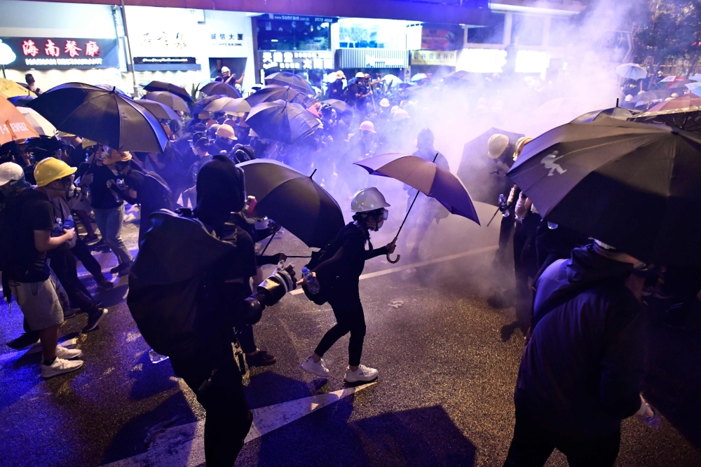 Protesters hold umbrellas as they are enveloped by tear gas on a street during a demonstration against a controversial extradition bill in Hong Kong on July 28, 2019. (AFP / Anthony WALLACE)
