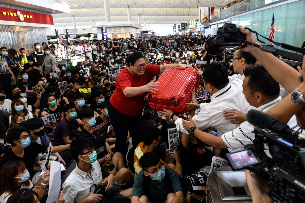 A tourist (C) gives her luggage to security guards as she tries to enter the departures gate during another demonstration by pro-democracy protesters at Hong Kong's international airport on August 13, 2019. (AFP / Philip FONG)
