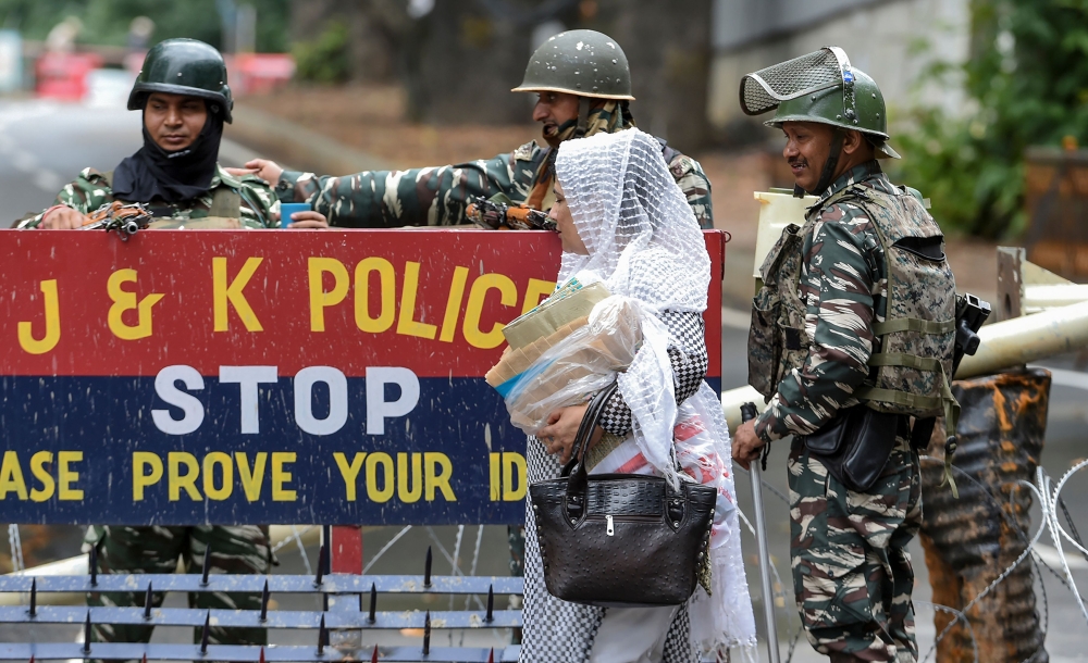 Indian security personnel stand guard as a Kashmiri woman walks past them in Srinagar on August 17, 2019.  AFP / TAUSEEF MUSTAFA