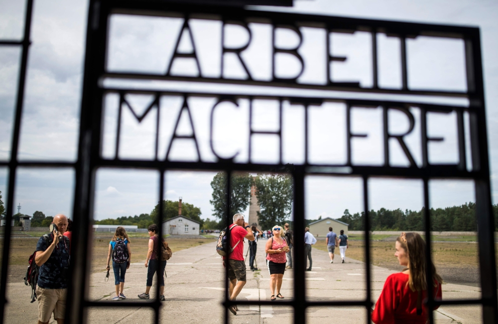 Visitors are seen through an iron gate carrying the German phrase 